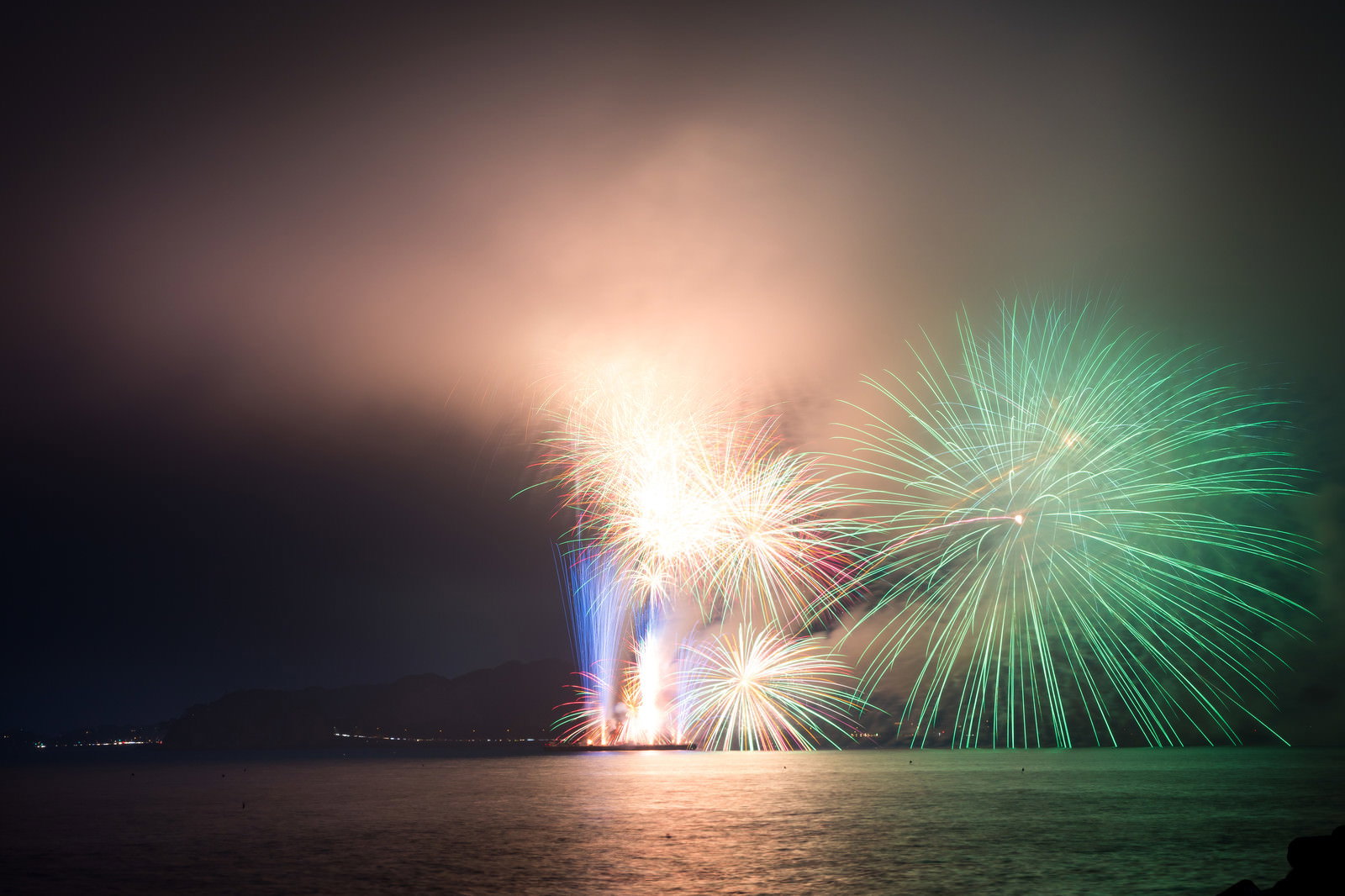 煙に包まれて光る花火大会のスターマインと夜空