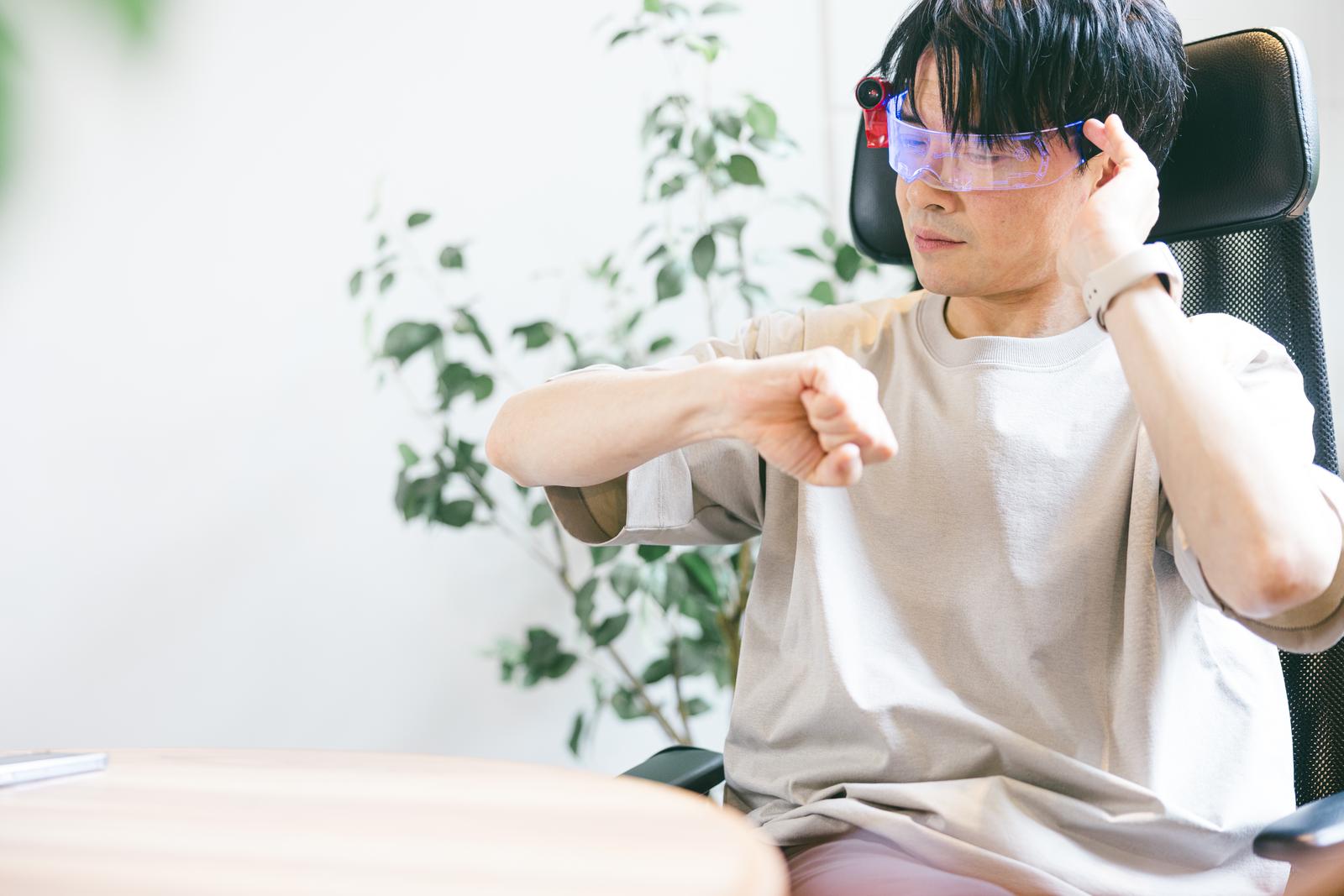 ARグラスを装着して腕時計の時間を確認するオフィスの男性［モデル：金子周平］