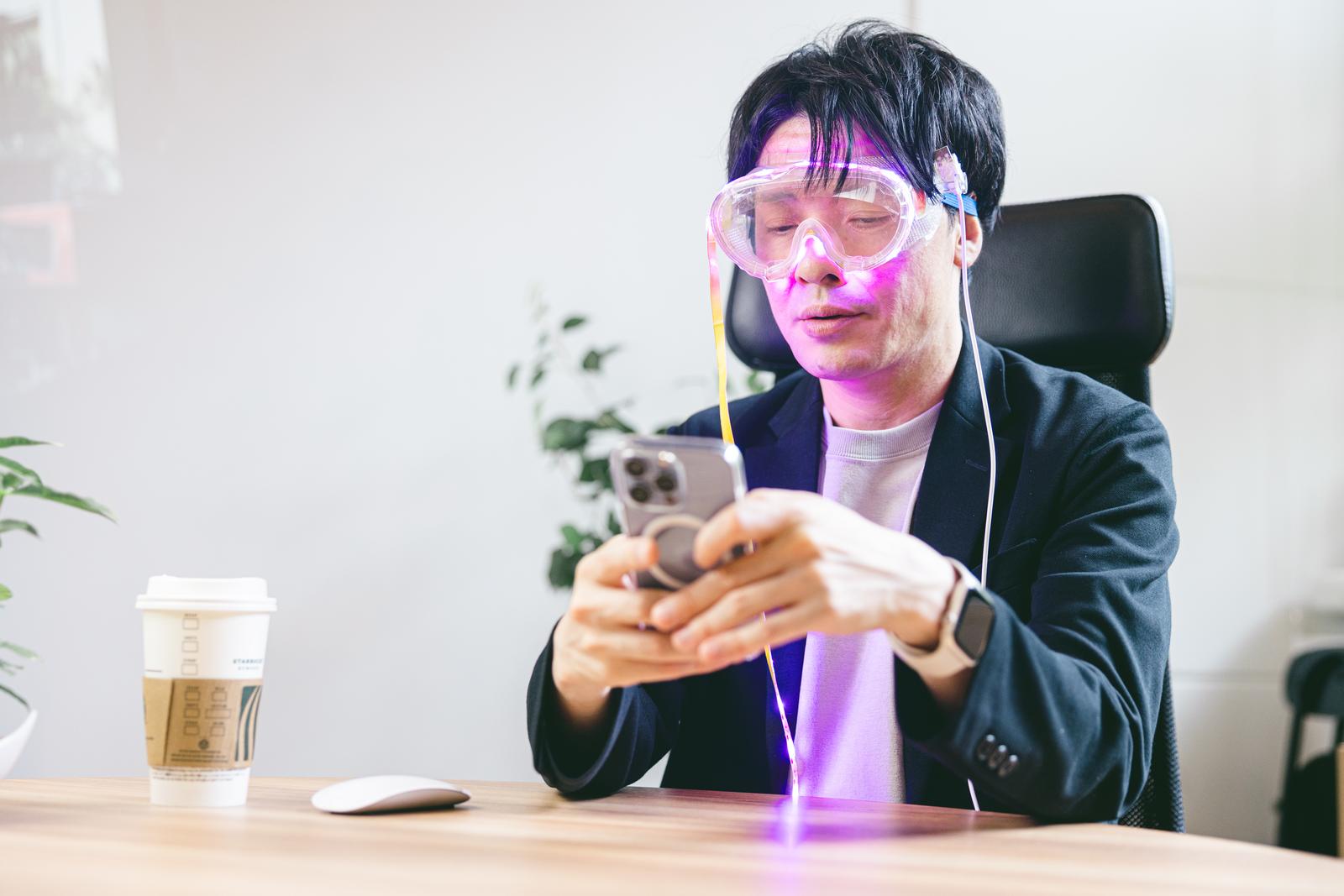 ピンク紫色のARゴーグルを装着してスマートフォンを操作する男性［モデル：金子周平］