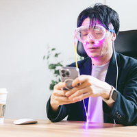 AR対応スマートゴーグルをつけてスマートフォンを操作する男性の写真