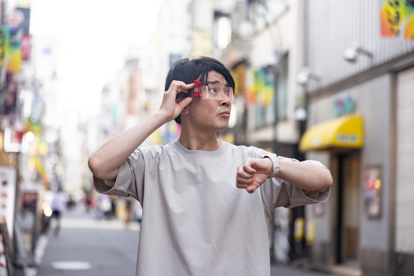 赤いARグラスをかけて空を見上げる男性が街中に立っている［モデル：金子周平］