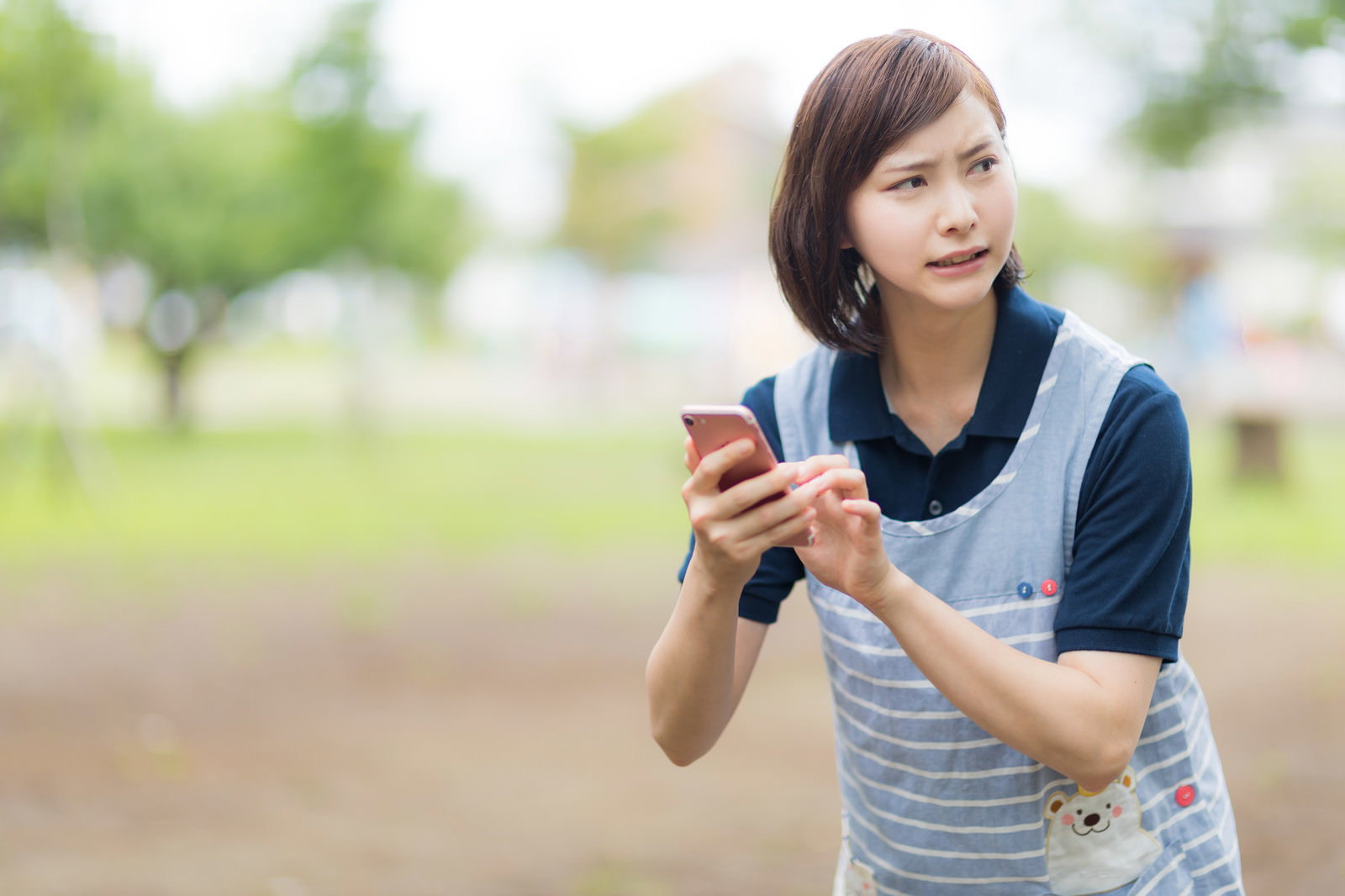 屋外でスマートフォンを持ちながら困った表情で周囲を見回す女性［モデル：yumiko］