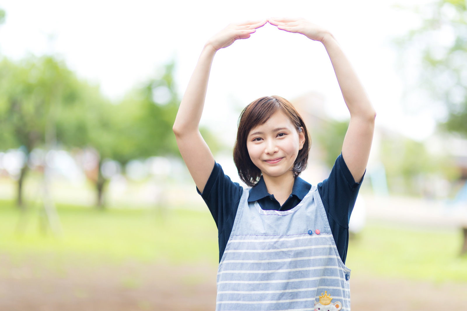 屋外で両手を頭上に上げてOKポーズをする笑顔の女性［モデル：yumiko］