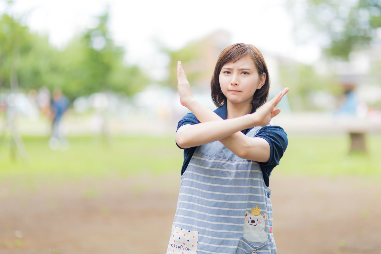 公園で両腕を交差させてバツサインを作る女性［モデル：yumiko］