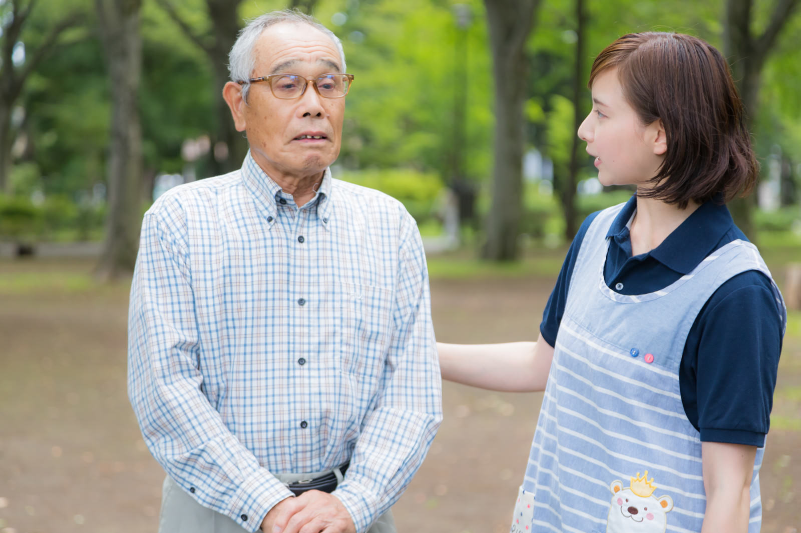公園の樹木前で向き合う高齢男性と女性介護士の会話風景［モデル：まーちゃん yumiko］