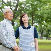 公園を散歩する高齢者と付添の介護士の外出支援の写真