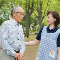 公園のベンチで寄り添うお爺さんと女性ヘルパーの写真