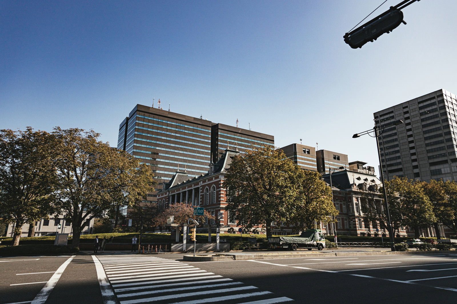 青空の下の法務省庁舎と手前に横断歩道が写った風景
