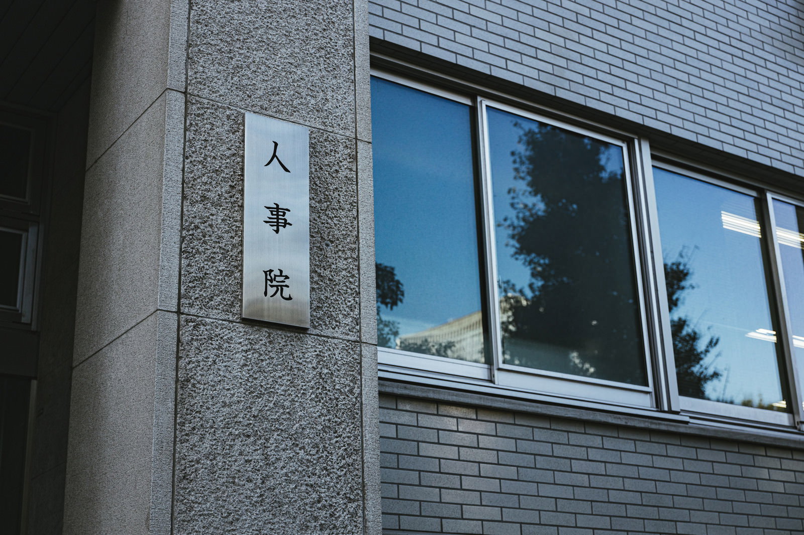 グレーの建物外壁に設置された人事院の白い銘板と窓