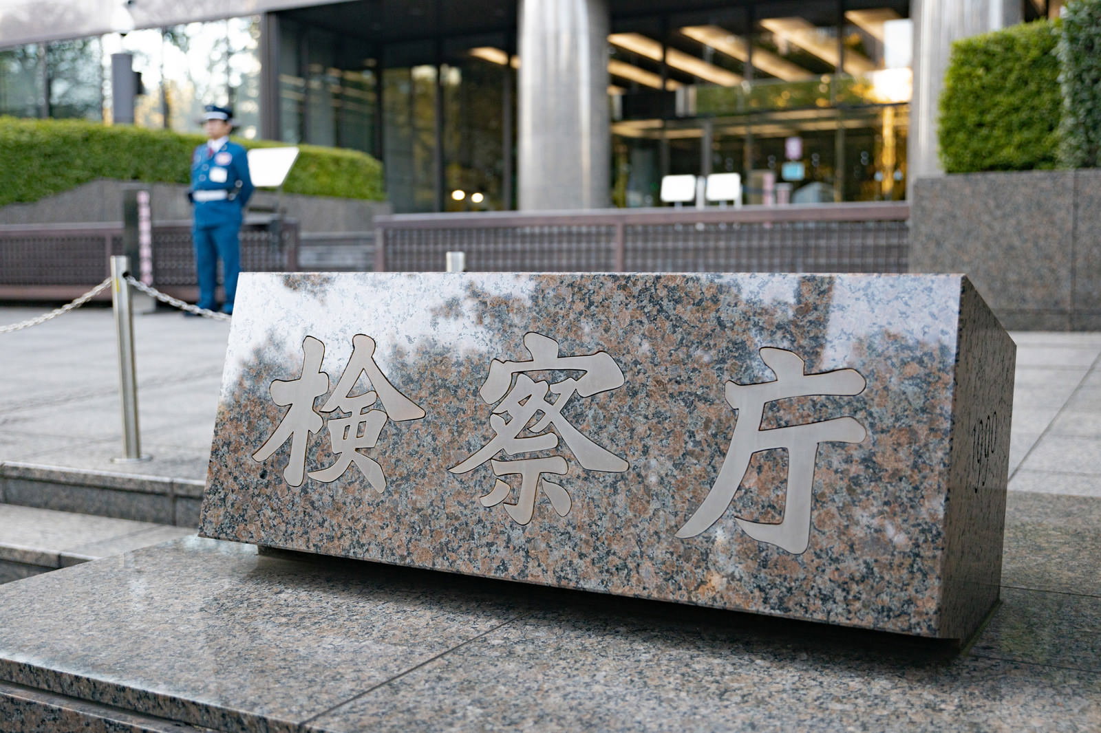 検察庁と書かれた石造の銘板と警備中の制服姿の守衛