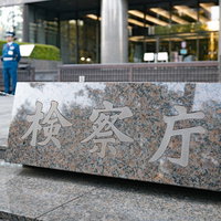 検察庁の石造銘板と守衛の制服、モダンな庁舎外観の写真