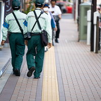緑と白の制服を着た駐車監視員が歩道を歩く後ろ姿の写真
