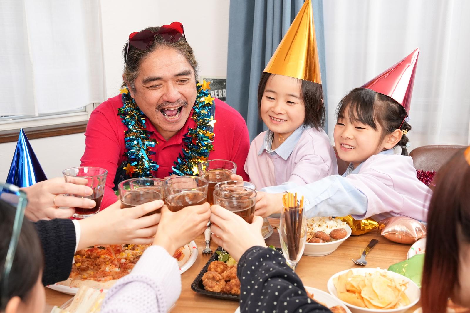 ホームパーティーで乾杯する父親と子どもたち、テーブルに料理が並ぶ［モデル：よたか あおみどり］