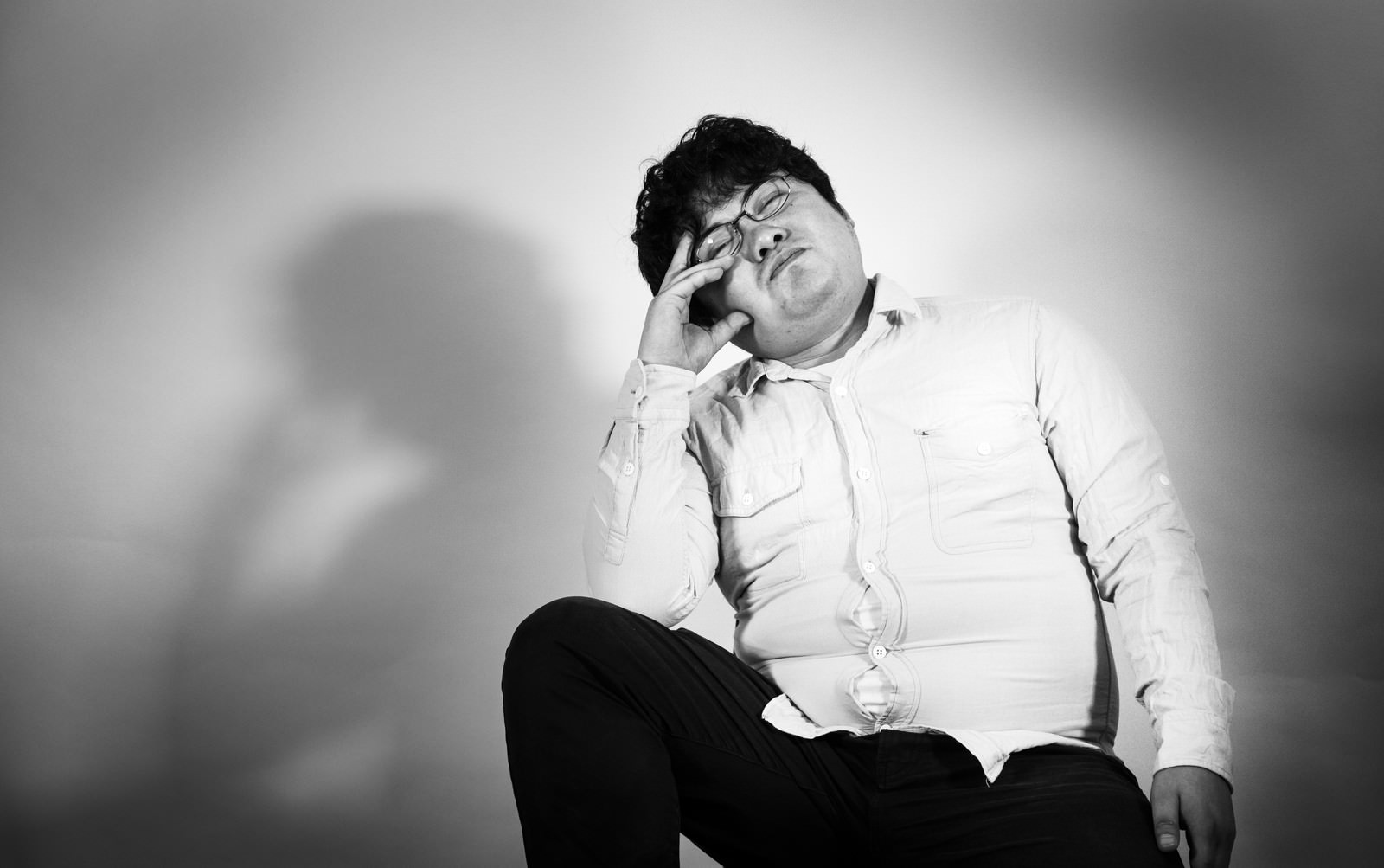 白いシャツを着た男性が椅子に座り頬杖をつくモノクロ写真［モデル：段田隼人］