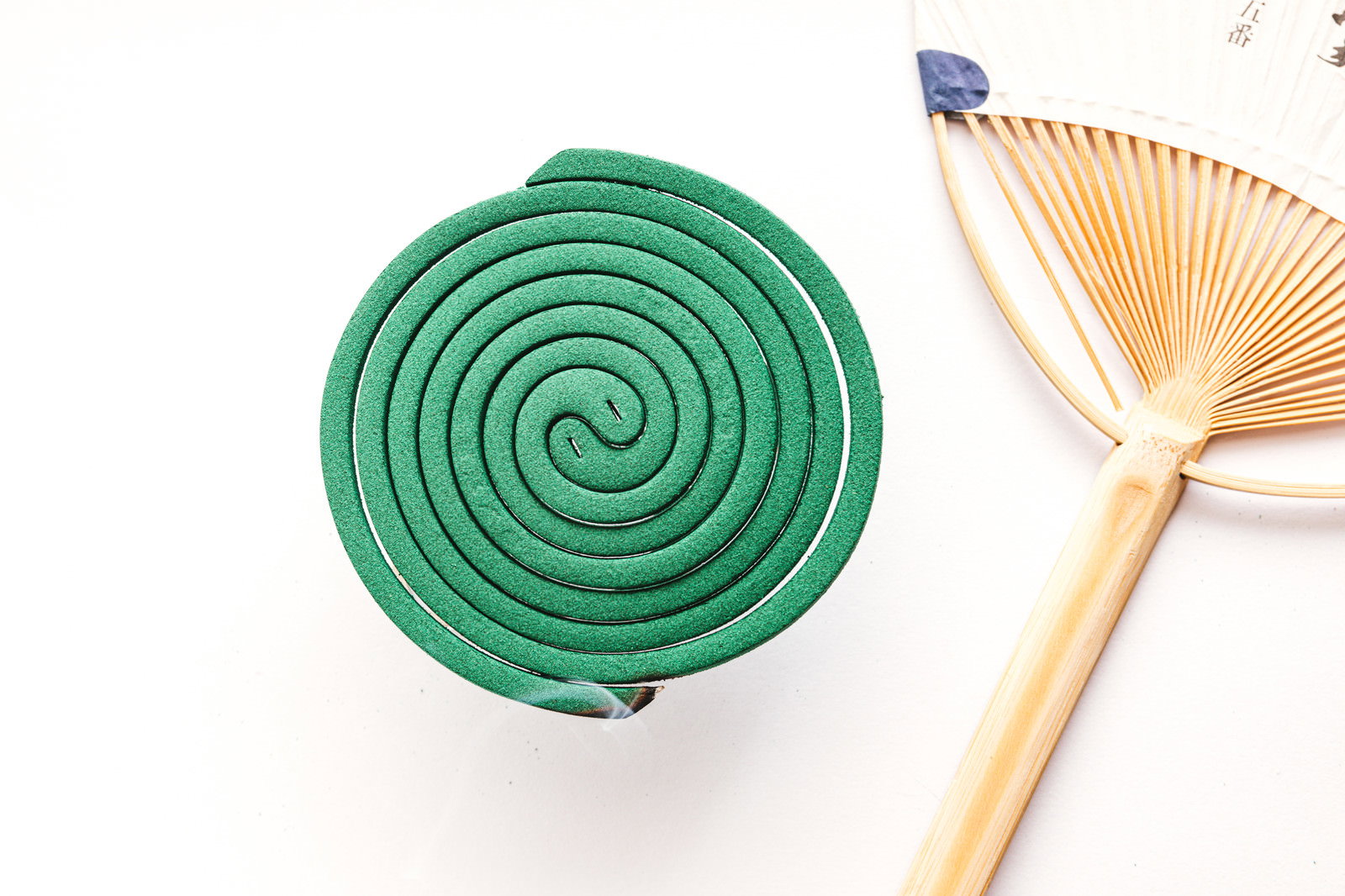 Green spiral-shaped mosquito coil and wooden fan placed on a white background