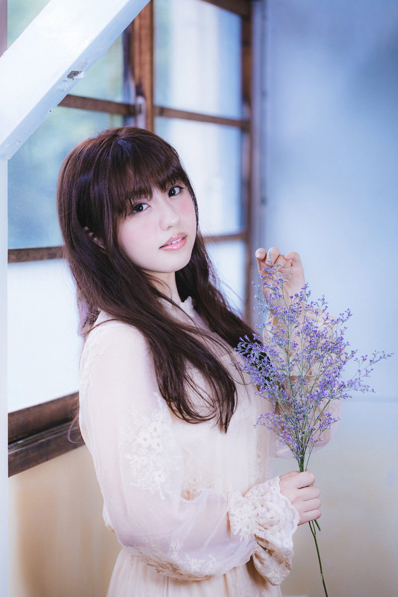 白い服を着た女性が室内で小さな花束を手に持ちレトロな窓辺でポーズをとる［モデル：河村友歌］
