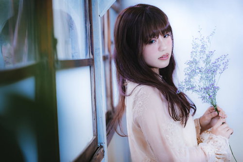 窓辺で遠くを見つめる悲しげな目つきの女性