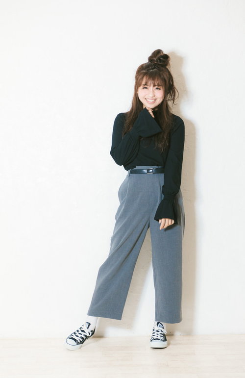 黒いトップスと水色のワイドパンツを着た笑顔の女子大生