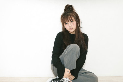 膝を抱えて座るうつろげな表情の若い女性、落ち込んだ様子