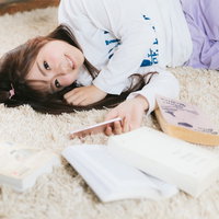 部屋着姿で本を読みながらカーペットでゴロ寝する女性の写真