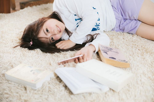 部屋着姿で本を読みながらカーペットでゴロ寝する女性