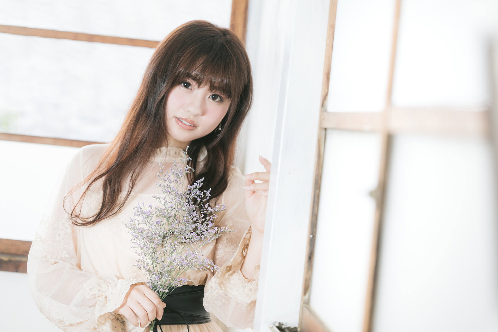白い服を着た長い髪の女性が室内で壁にもたれかかっている［モデル：河村友歌］