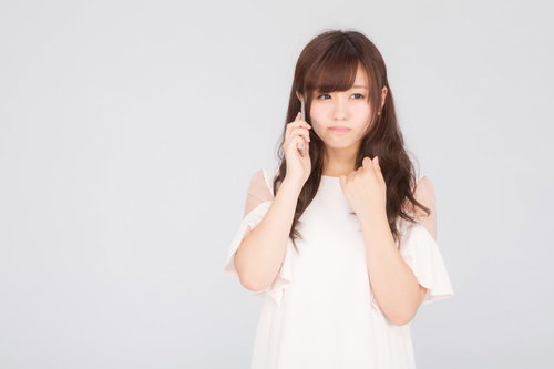 残念なお知らせを聞いてスマホ通話中に落ち込む女性