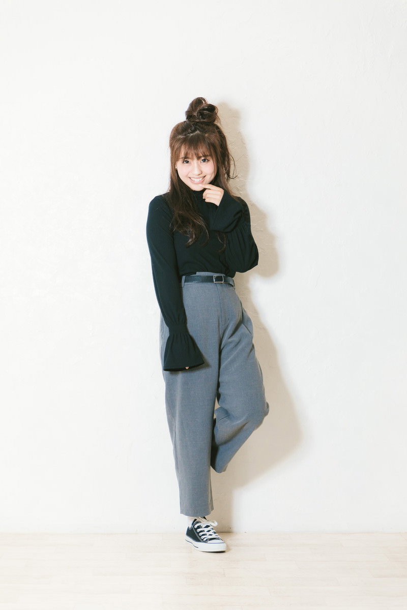 緑色のトップスとデニムのワイドパンツを着た女性が壁にもたれて笑顔でポーズしている［モデル：河村友歌］