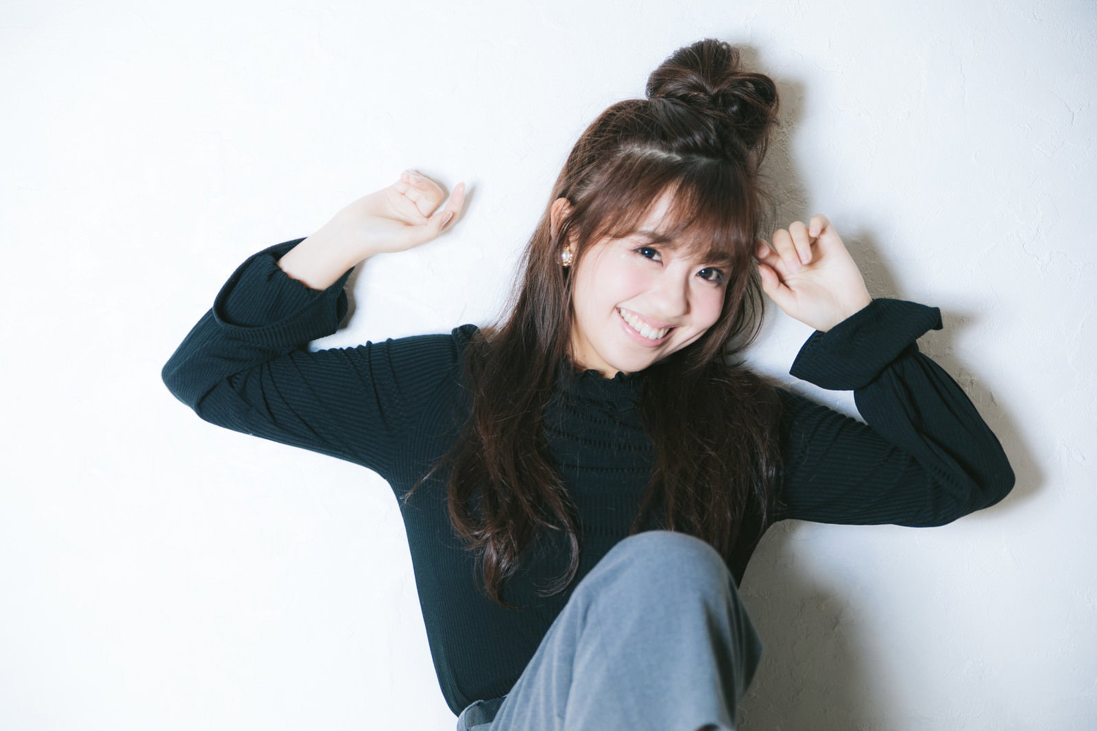 壁にもたれかかって笑顔でポーズを取る女性［モデル：河村友歌］