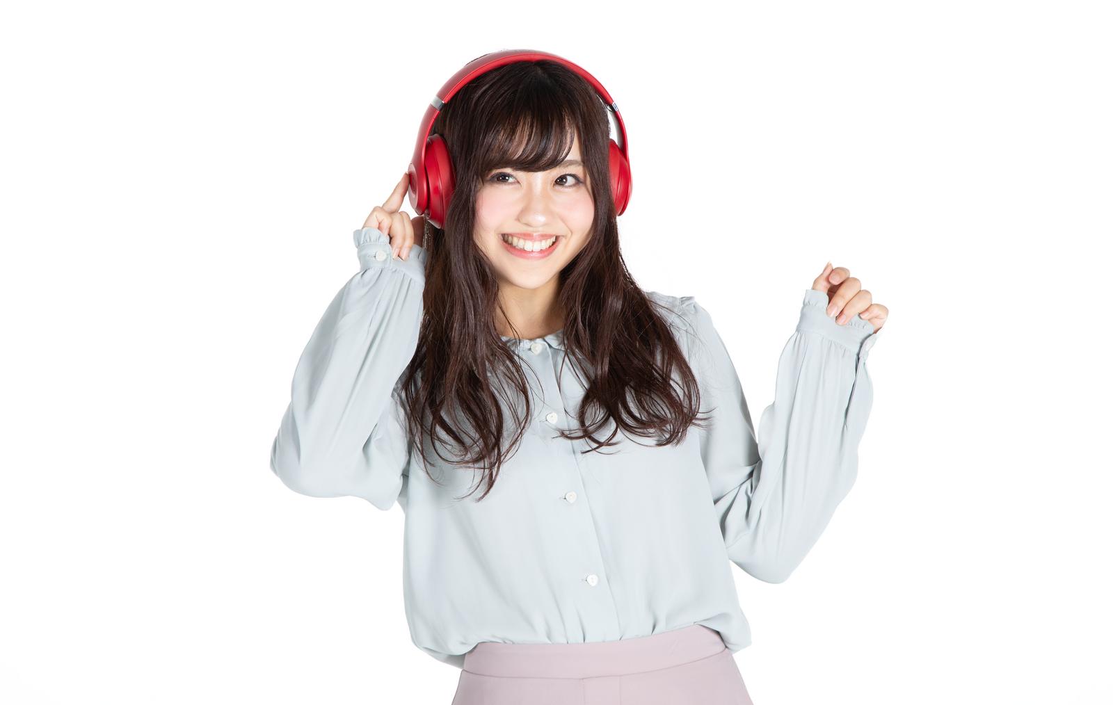 赤いヘッドフォンをつけて音楽を聞きながら笑顔で両手を上げる女性［モデル：河村友歌］