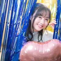 青と黄色の装飾の中から顔を出して微笑む女性の写真