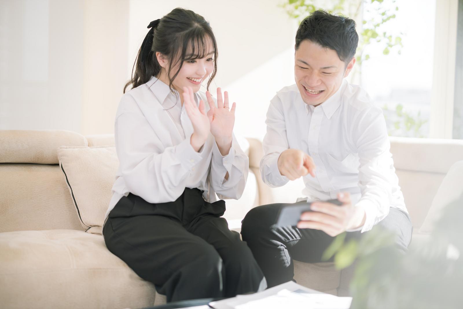 スマートフォンの画面を見ながら両手を振って笑顔で応援する女性社員［モデル：河村友歌 モデルリリース］