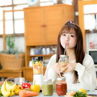 朝スムージーを楽しむ女性、キッチンで野菜と果実から作るヘルシードリンクの写真