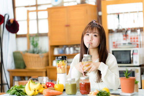 朝スムージーを楽しむ女性、キッチンで野菜と果実から作るヘルシードリンク