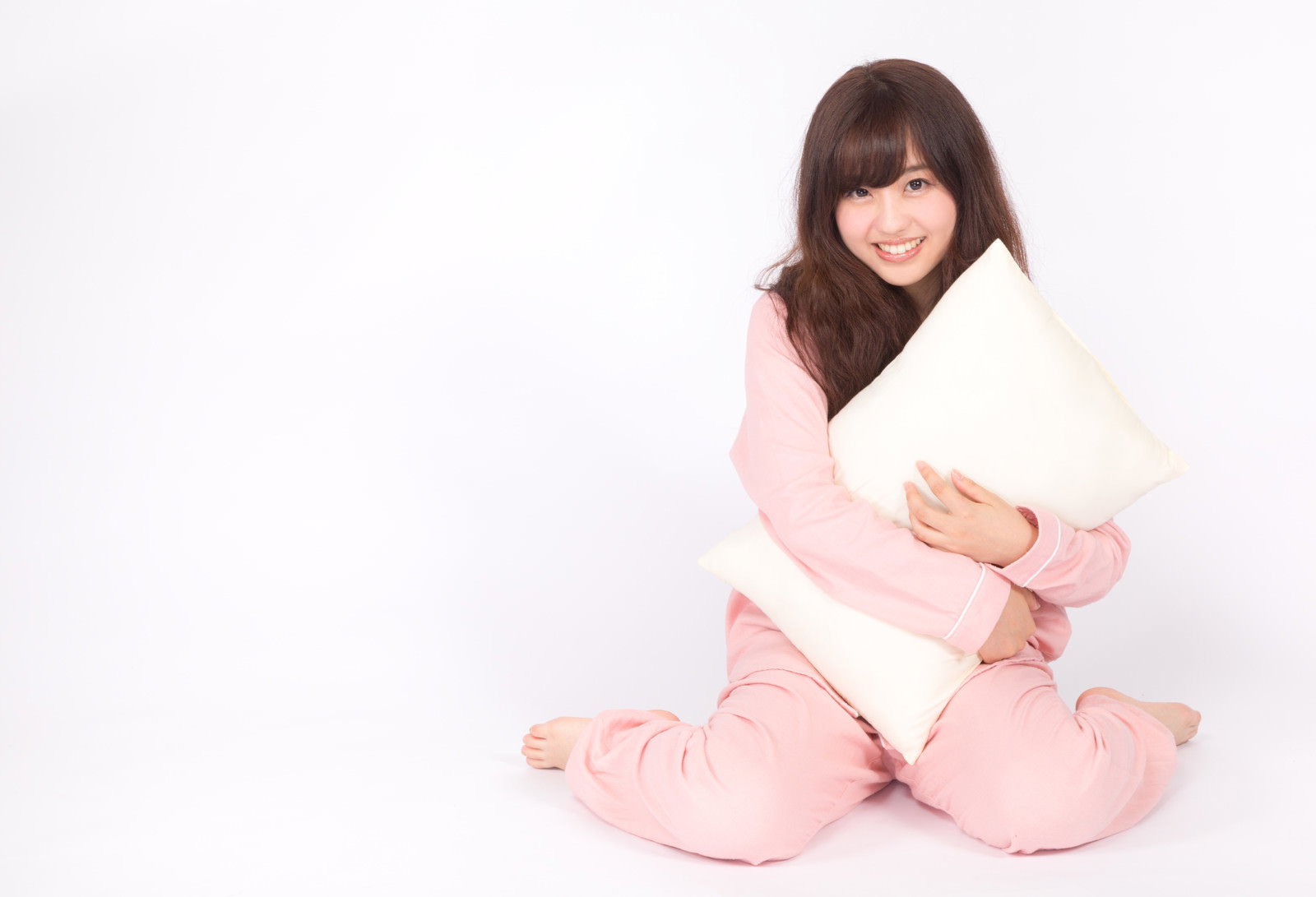 ピンクのパジャマを着て白い枕を抱きしめて座る女性