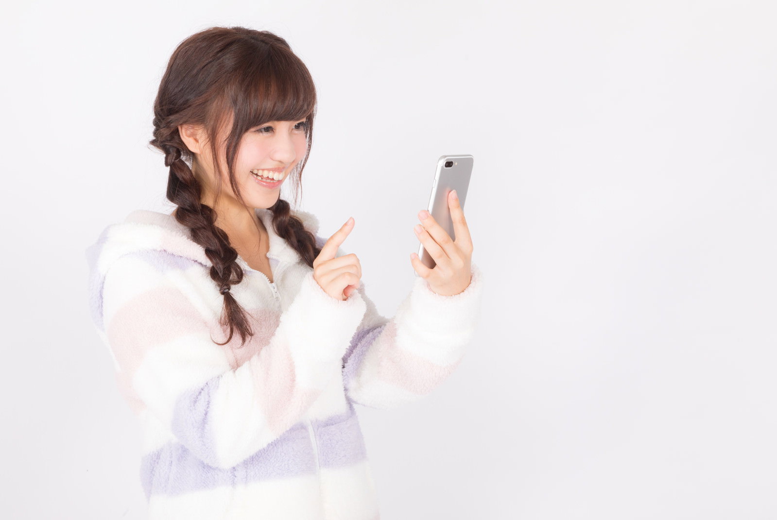 白い背景の前で笑顔でスマートフォンを操作する女性［モデル：河村友歌］