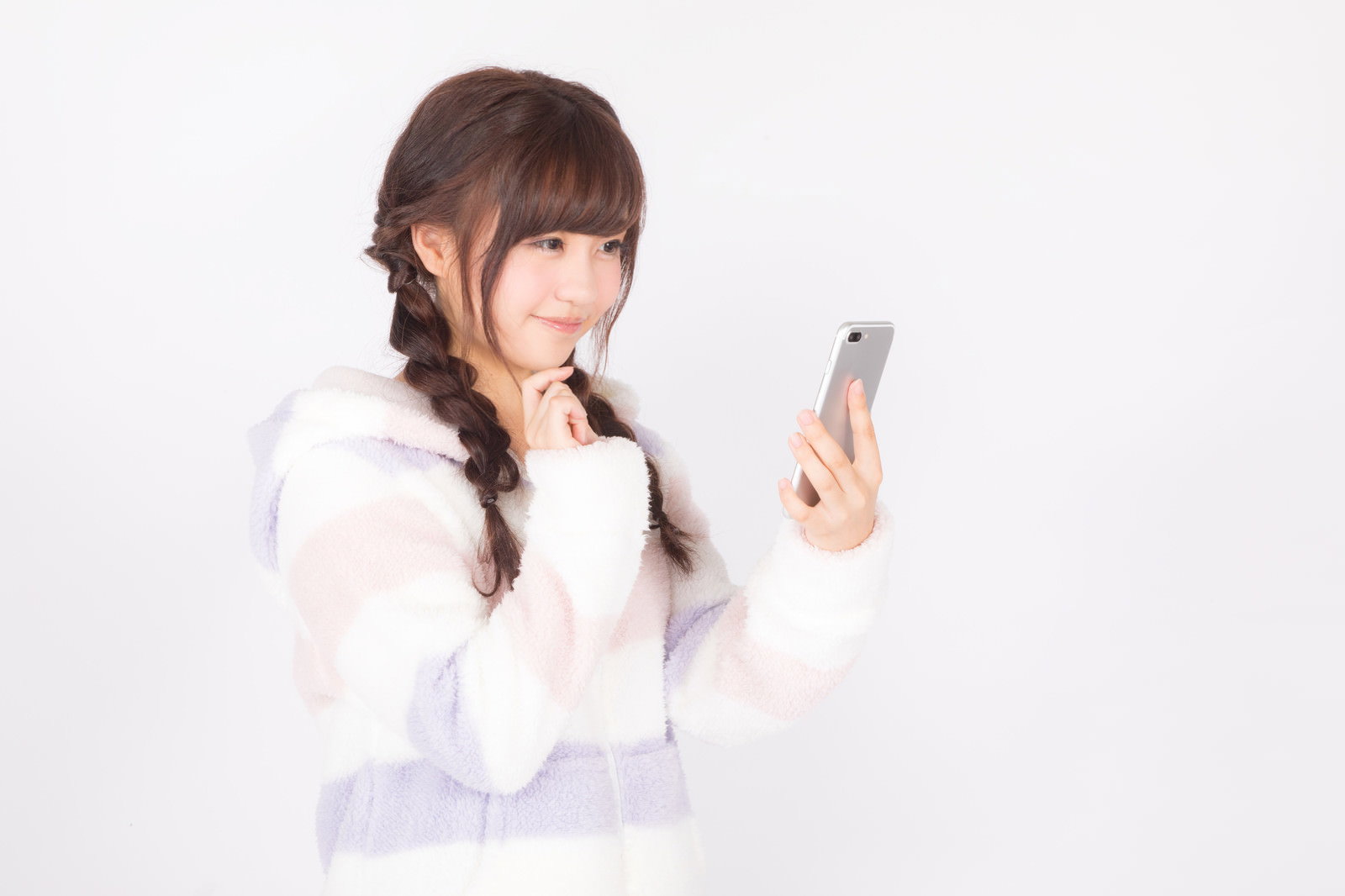 白い背景でスマートフォンを手に持ち笑顔を見せる女性［モデル：河村友歌］