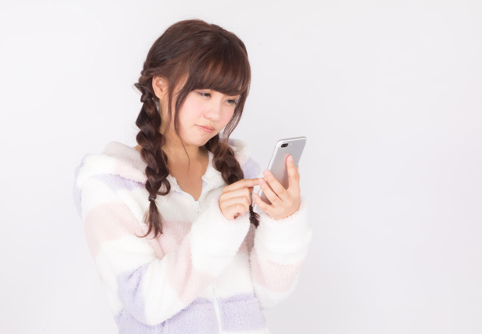 白いパジャマを着た女性がスマートフォンを見つめ困った表情を浮かべている［モデル：河村友歌］