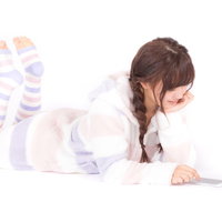 パジャマ姿で横になりながらスマホアプリを楽しむ女性の写真