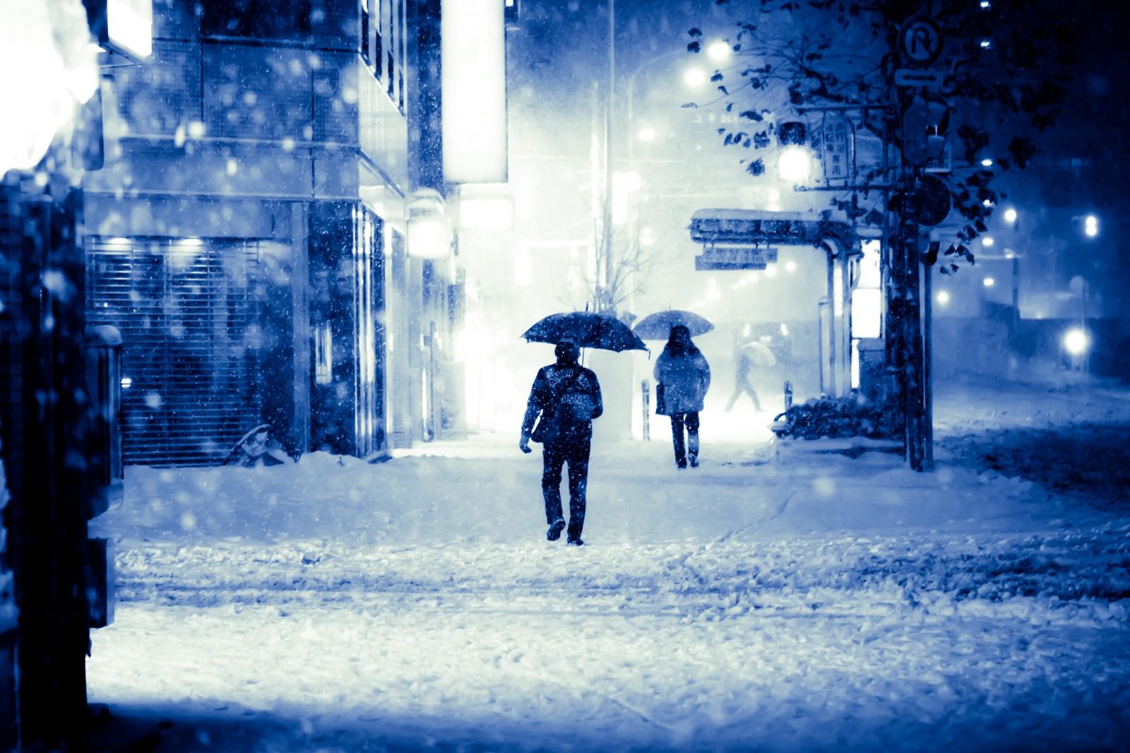 大雪の夜に傘を差して雪道を歩く人