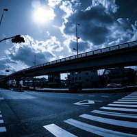 太陽が雲の隙間から差す都市の高架道路と横断歩道のある交差点の写真