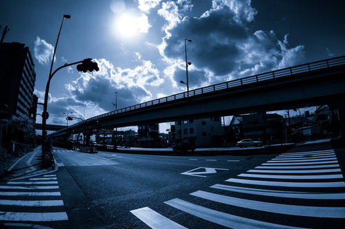 太陽が雲の隙間から差す都市の高架道路と横断歩道のある交差点