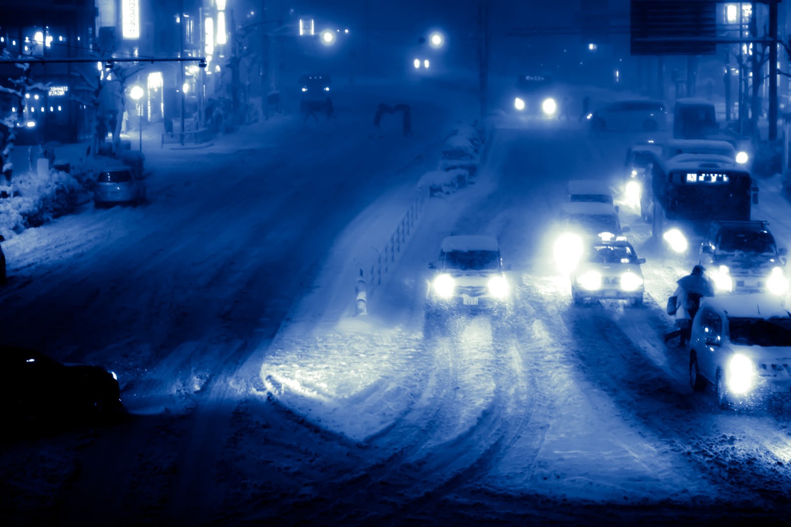 雪が積もった夜の街中を走る車のヘッドライトが連なる幹線道路