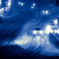 雪が積もった夜の街中を走る車のヘッドライトが連なる幹線道路の写真