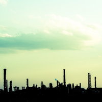 緑がかった空に煙突や塔が並ぶ工場のシルエットの写真