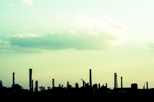 緑がかった空に煙突や塔が並ぶ工場のシルエット