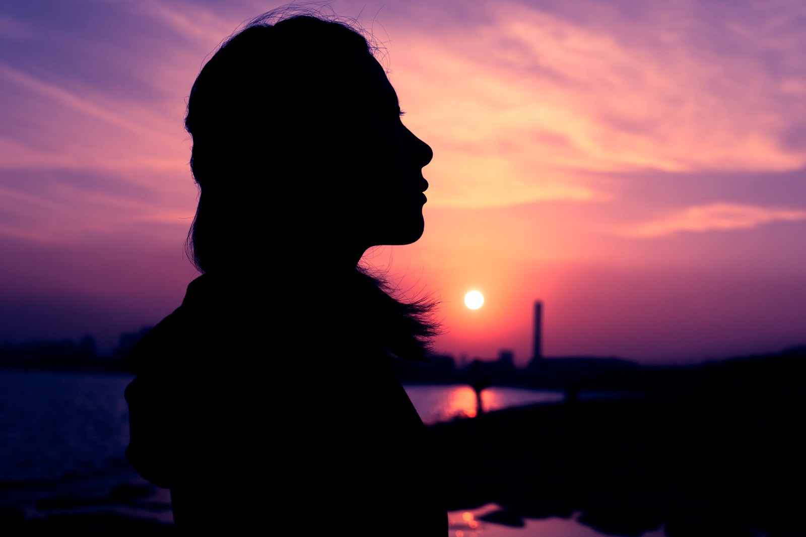 紫色の夕焼け空を背景に女性の横顔がシルエットで映る写真［モデル：Mizuho］
