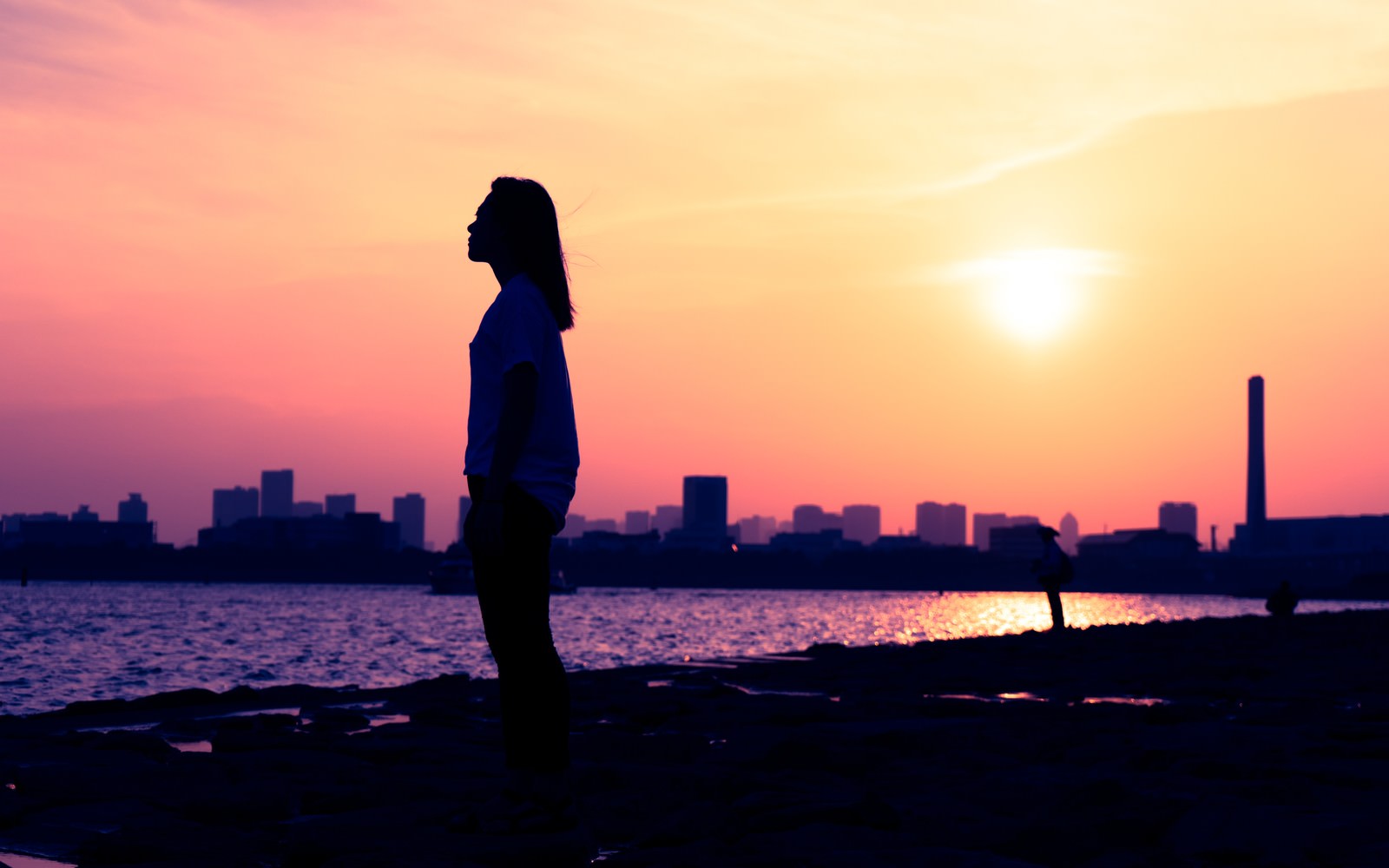 夕焼け空を背景に立つ女性のシルエットと都市の風景［モデル：Mizuho］