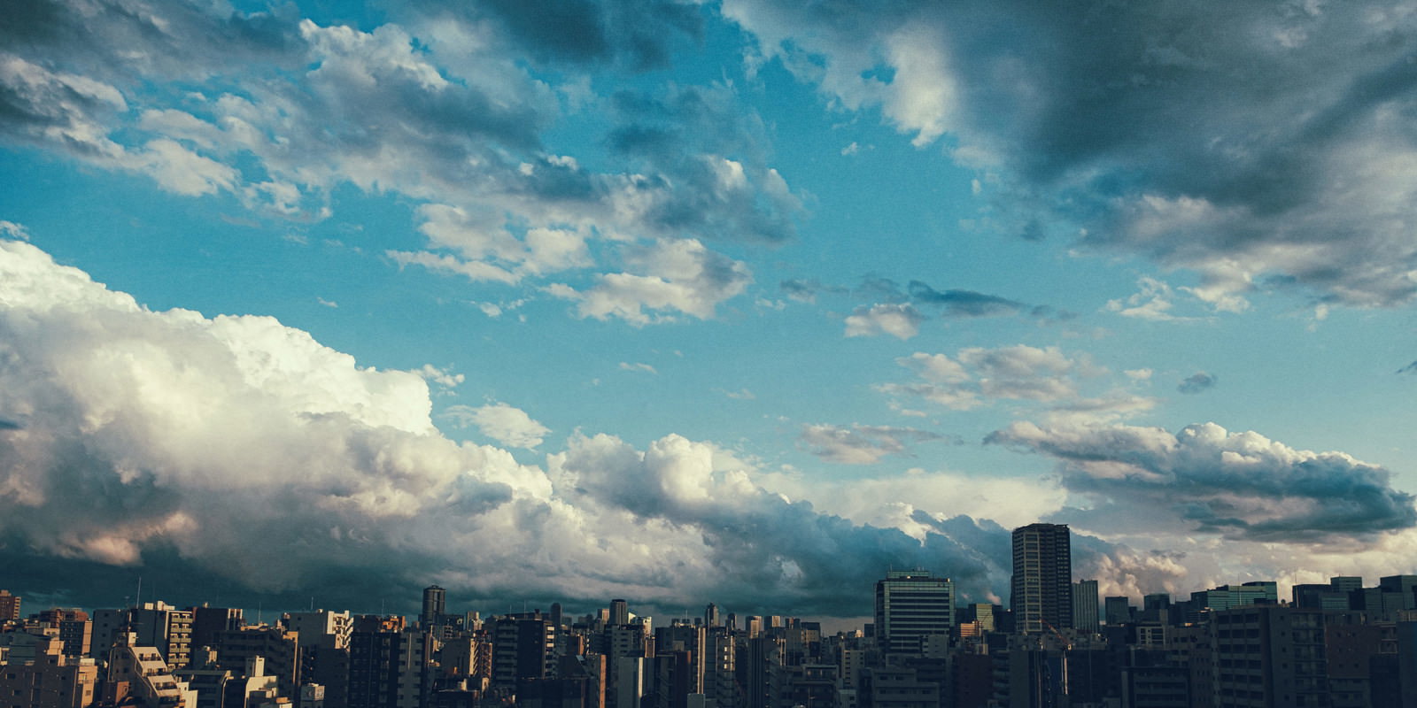 上空に晴れ間と雨雲が広がる都心の街並み風景