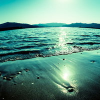 波打ち際に反射する日の光と砂浜、山並みと太陽光のラインの写真